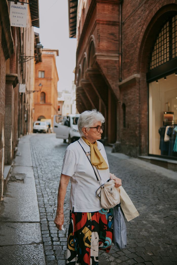 Senior woman with a scarf walking in a historic European city street with cobblestones and renaissance architecture.