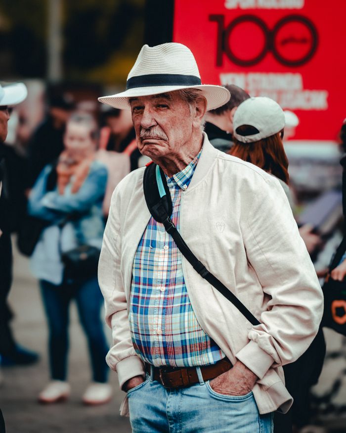 Portrait of senior man wearing a hat at an outdoor gathering, showing emotion.