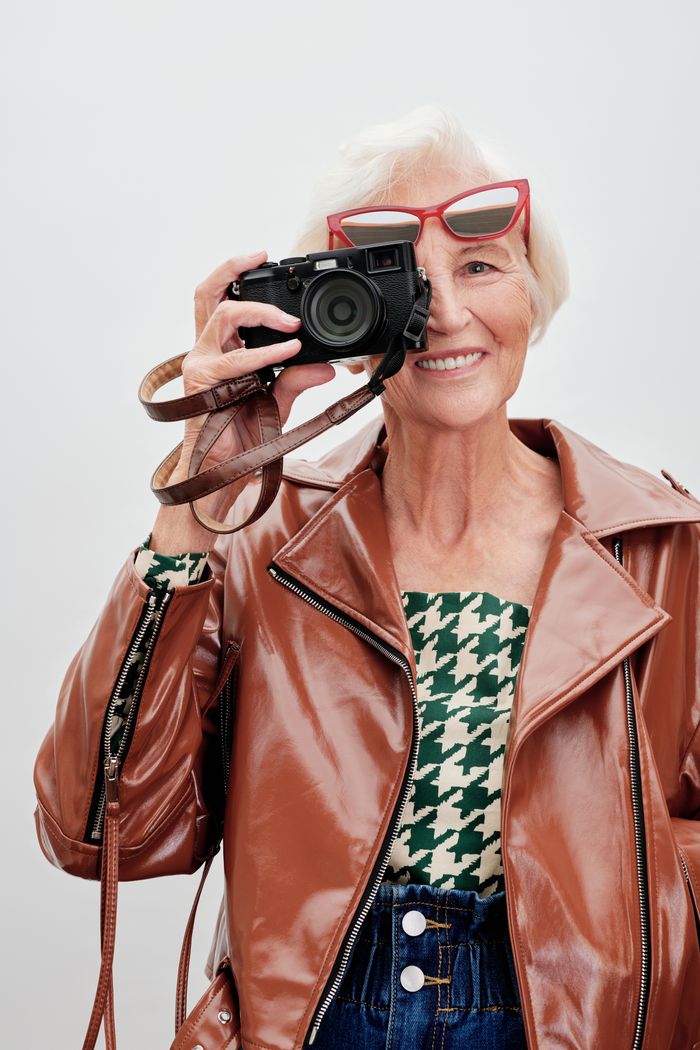 Fashion-forward senior woman with a camera in leather jacket and red glasses.