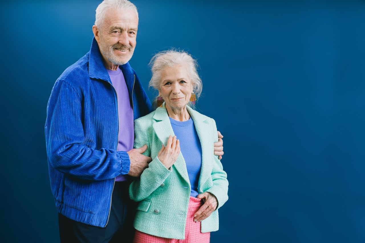 Senior couple posing confidently in stylish outfits against a blue backdrop.