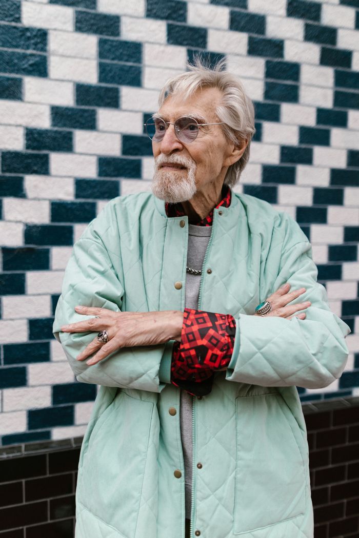 Fashionable senior with glasses poses confidently against brick wall, showcasing street style.
